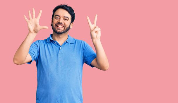 Giovane uomo ispanico indossa abiti casual mostrando e indicando con le dita il numero sette sorridendo fiducioso e felice.  - Foto, immagini