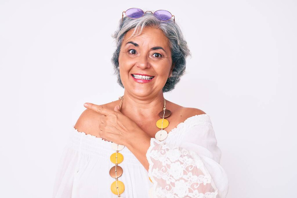 Ältere hispanische grauhaarige Frau in lässiger Hippie-Kleidung lächelt fröhlich und zeigt mit der Hand und dem Finger zur Seite  - Foto, Bild