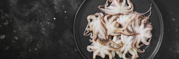 Octopus in the dish. Small octopuses in a large black plate on the black kitchen table. Lots of little raw octopuses. The view from the top. Banner with space for text - Фото, изображение