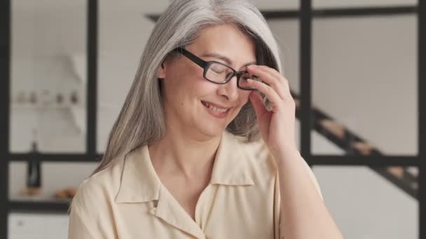A smiling old woman is putting of her glasses and looking to the camera in the living room at home - Filmmaterial, Video