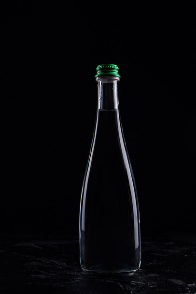 Бутылка с темной жидкостью на черном фоне
. - Фото, изображение