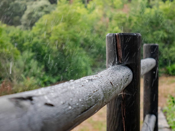 Water druppels crashen en spatten op een houten hek in een landhuis op een regenachtige dag - Foto, afbeelding