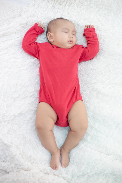 ベッドで寝てる赤いシャツを着た赤ん坊 - 写真・画像