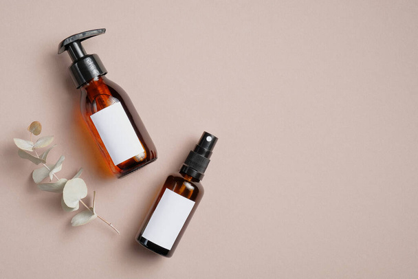 Amber glass cosmetic bottles and eucalyptus leaves on brown background. SPA bathroom natural cosmetic packaging mockup. Flat lay, top view. - Photo, image