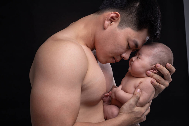 The baby sleeps in the hands of a strong father. - 写真・画像