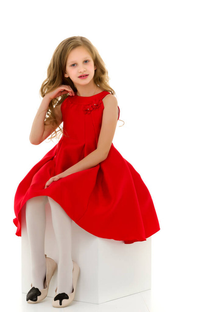 Portrait of Lovely Girl in Stylish Red Dress Sitting on White Cub. - Foto, afbeelding