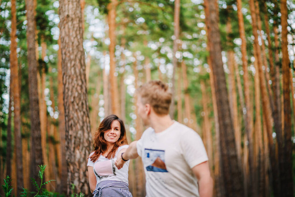 A young active couple of young people hold each other's hands while taking a walk through a pine forest, one of the lovers blurred - Foto, Bild