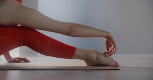 Giovane donna in tuta rossa seduta sul tappeto yoga e appoggiata in avanti ai suoi piedi, persona fa allenamento fisico, stretching yoga e ginnastica, 4k 120p Prores HQ 10 bit - Filmati, video