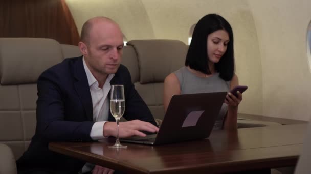 Close-up van een jong paar een zakenman Werken op een computer een vrouw met behulp van een smartphone In haar eigen privé-vliegtuig een Business Jet - Video