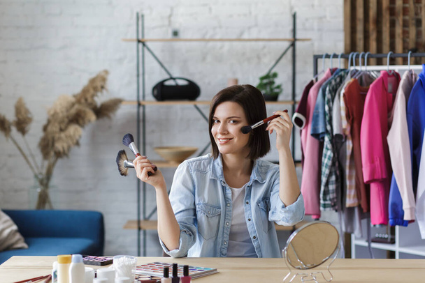 Young female blogger recording a tutorial video for her beauty blog about cosmetics.Vlogger testing face powder and broadcast live video to social network at home.Blogging, videoblog, makeup concept - Foto, Imagem