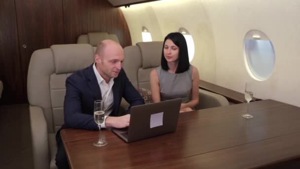Jeune couple homme femme travaillant à un ordinateur discutant d'un nouveau projet boire du champagne, voler un jet privé d'affaires - Séquence, vidéo