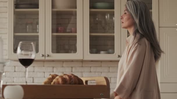 A calm pretty nice mature woman is walking in the kitchen at home in the morning - Materiał filmowy, wideo