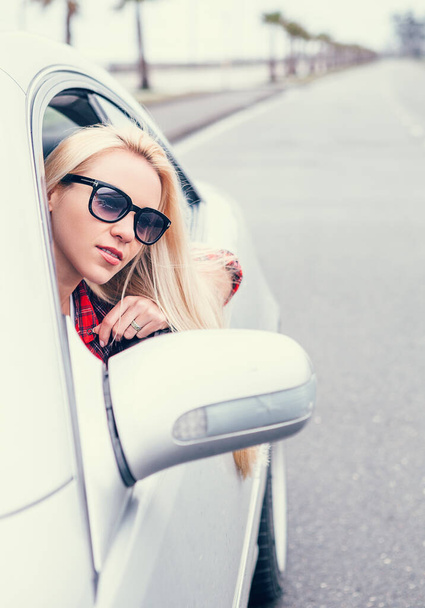 Pretty young blonde woman looks out from car window - Photo, Image