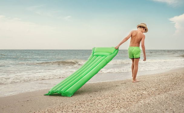 Boy with swimming mattress walks on sand sea beach - Фото, изображение