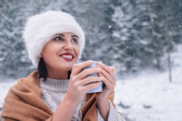 Woman with cup of hot tea on snowy forest background - Фото, зображення