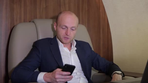 スマートフォンを使って仕事をしている若いビジネスマンの閉鎖自分の個人的な飛行機ビジネスジェットで電話で話すビジネスをしている - 映像、動画