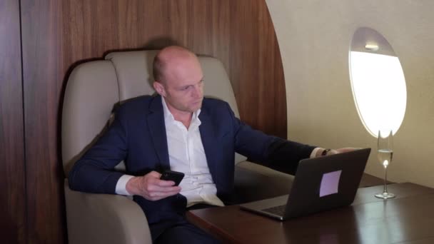 Close Up of a Young Businessman Working Using a Smartphone Doing Business Talking on the Phone Drinking a Glass of Champagne Flying in his own Personal Plane Business Jet - Záběry, video