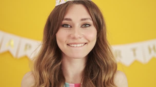 A cheerful nice birthday-woman is blowing confetti to the camera standing isolated over a yellow background - Záběry, video