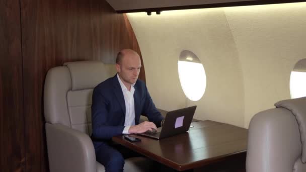 Jovem empresário trabalhando usando um laptop de computador fazendo negócios voando em seu próprio avião pessoal jato de negócios
 - Filmagem, Vídeo