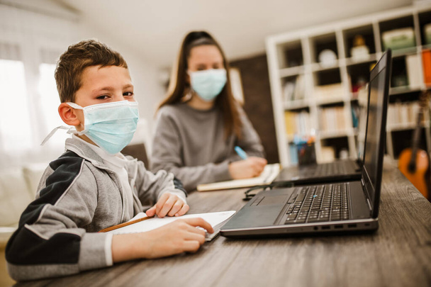 Boy and girl studies at home, wear protective masks, and doing school homework. Distance learning online education. - Fotó, kép