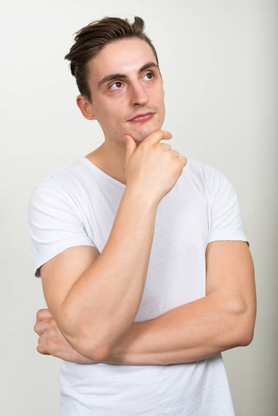 Studio shot of young handsome man with brown hair against white background - Foto, imagen