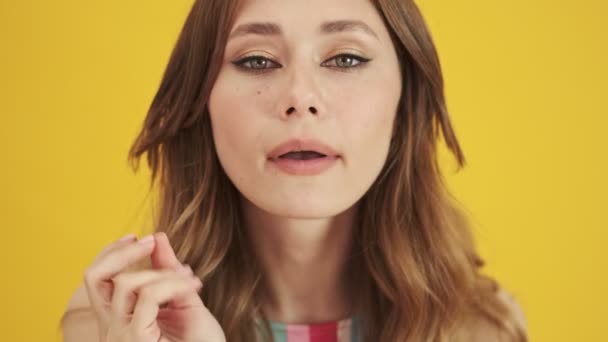 A close-up view of a pretty nice young woman is touching her lips while looking to the camera like to the mirror isolated over a yellow background - Imágenes, Vídeo