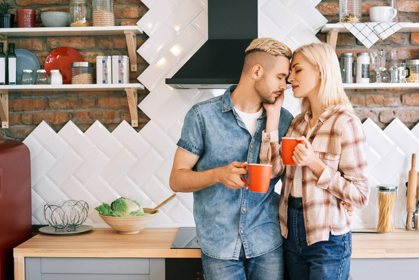 Young happy couple in love drink coffee in the morning embracing in kitchen at home - Foto, Bild