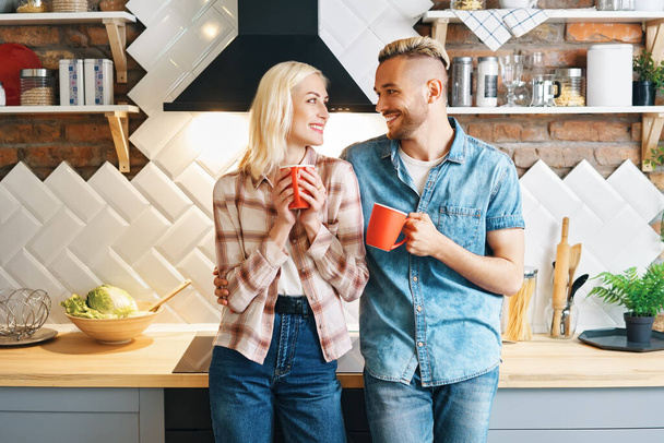 若い幸せなカップルは午前中にコーヒーを飲み、自宅でキッチンでお互いの会社を楽しむ - 写真・画像