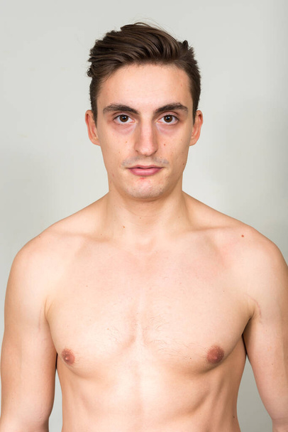 Студійний знімок молодого красивого м'язистого чоловіка з коричневим волоссям без сорочки на білому тлі
 - Фото, зображення