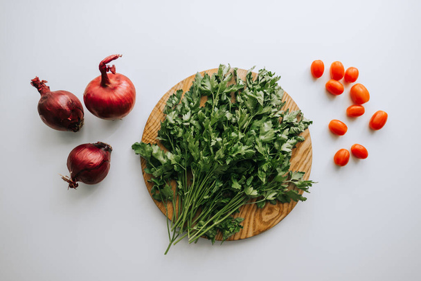 Green parsley on a wooden board, red onion and cherry tomatoes, white background. Proper nutrition. Flat lay. High quality photo - Foto, Imagem