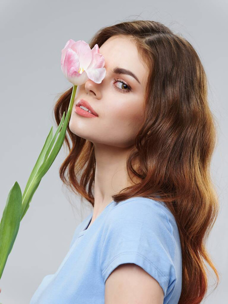 Eine charmante Dame mit einer rosa Blume in der Nähe ihres Gesichts  - Foto, Bild