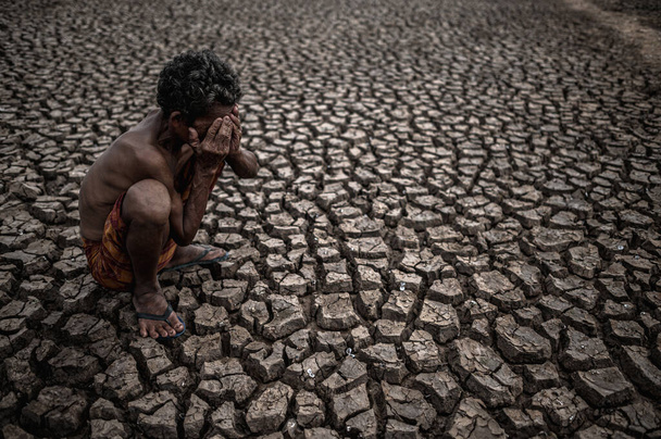 Na suché zemi seděl postarší muž se sehnutými koleny a rukama sevřenýma na tváři, globální oteplování - Fotografie, Obrázek