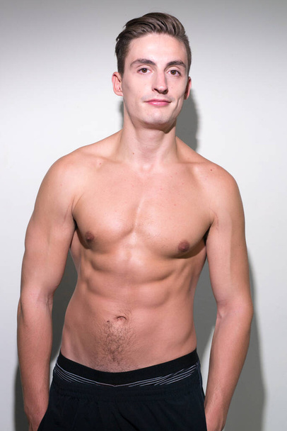 Studio shot of young handsome muscular man with brown hair shirtless against white background - Foto, imagen