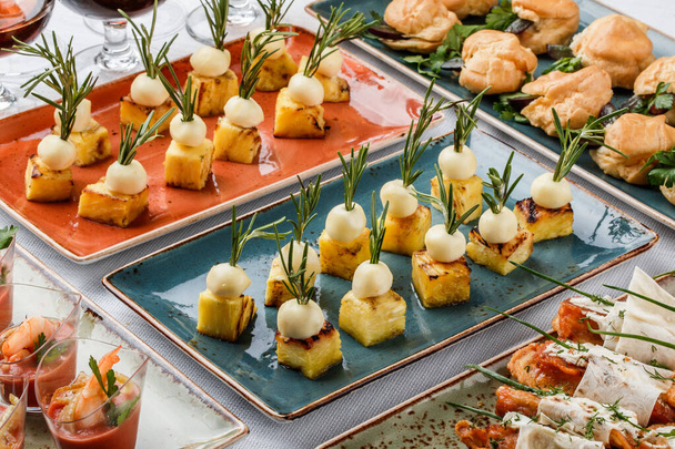Herkullisia alkupaloja juustolla ja ananaksella lautasella juhla-pöydällä. Ateriapalvelut, kanapit ja välipalat - Valokuva, kuva