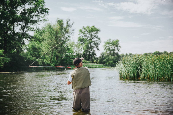 Mladý rybář rybaří na jezeře nebo řece. Zadní pohled na muže siluetu v řece nebo jezeře vody se snaží chytit ryby. Používám rybí prut na lov. Slunečný letní den. - Fotografie, Obrázek