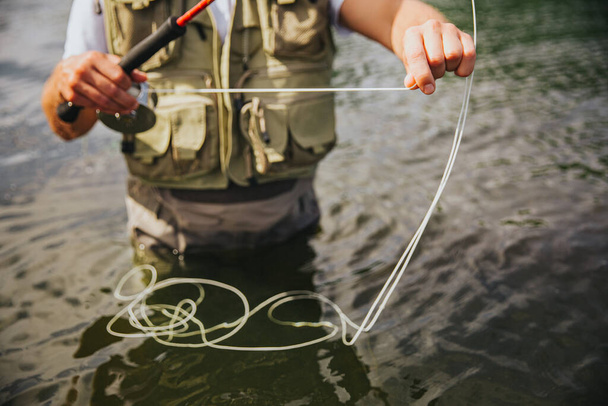 湖や川で若い漁師釣り。水の中に一人で立って、手にいくつかの釣り糸を保持男のカットビュー。漁期に備える設備. - 写真・画像