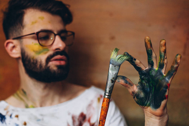 Porträt eines jungen kreativen Künstlers: Ein Mann hält einen großen Pinsel mit Farbe in der Hand. Kopierraum - Foto, Bild