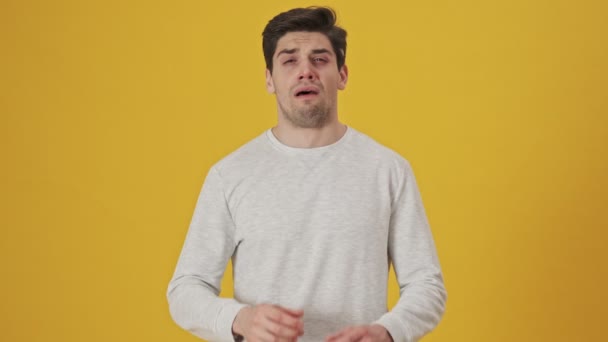 Unhappy sick man with runny nose sneezing and looking at the camera over yellow background - Кадри, відео
