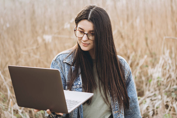 Happy hipster young woman working on laptop in field. Outdoors nature journey and relaxation. Freelance work concept. - Φωτογραφία, εικόνα
