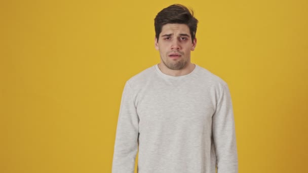 Displeased sick man showing gun gesture and looking at the camera over yellow background - Séquence, vidéo