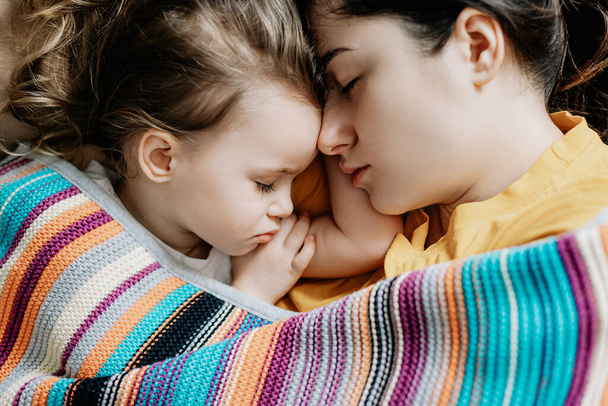 Young mother and baby of 2 years sleep together hugging, daytime sleep concept for children. Mom fell asleep with her baby while putting her to sleep - Фото, изображение