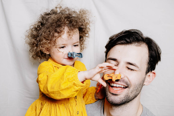 father and daughter. Young pretty dad and his little curly daughter hugging and having fun at home against the background of a makeshift photo studio - 写真・画像