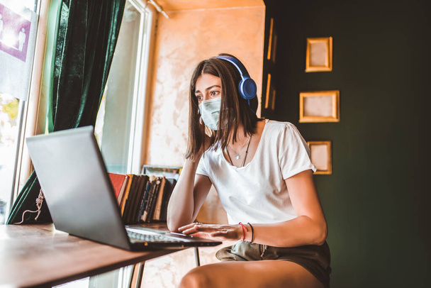 Випадкова жінка фрілансер в масці для обличчя, навушники, що використовують ноутбук для дистанційної роботи в Інтернеті в кафе
 - Фото, зображення