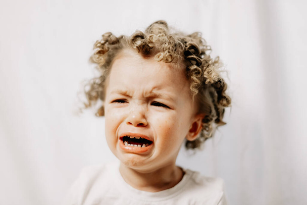 Little curly girl is crying very emotionally, face with tears and negative emotions of disappointment and insult. Baby emotions and baby crying - Фото, зображення
