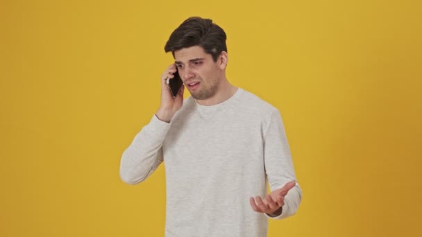 Serious sick man talking by smartphone then becoming displeased and screaming over yellow background - Záběry, video