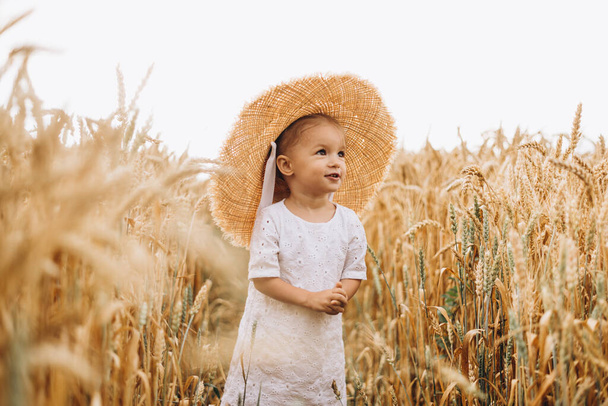 pretty cute baby girl with a beautiful smile wearing summer straw hat in a walk in the  wheat fields. selective focus. family, people concept - Foto, immagini