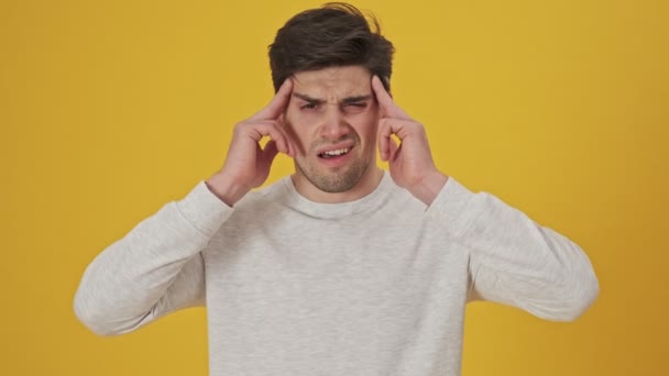 Unhappy sick man touching her temples while having headache over yellow background - Filmati, video