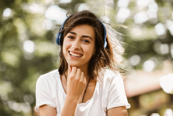 Chica emocionada escuchando música con auriculares en la calle con el pelo en movimiento
 - Foto, Imagen