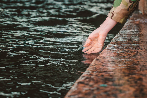 Das Mädchen tauchte ihre Hand ins Wasser. Mit der Handfläche den Fluss berühren, während man die Böschung entlanggeht - Foto, Bild