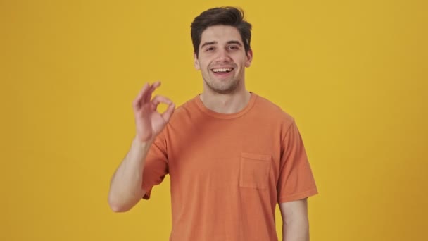 笑顔ハンサムな男身に着けていますでtシャツショーok signジェスチャーでザカメラ上の黄色の背景 - 映像、動画